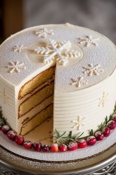 a white cake with a slice cut out of it on a silver platter covered in snowflakes and cranberries