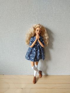 a doll with blonde hair is standing on a wooden table next to a white wall