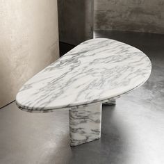 a white marble table sitting on top of a metal floor next to a gray wall