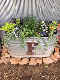 a metal tub filled with lots of plants next to a wall and some rocks on the ground