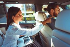 a woman sitting in the back seat of a car with a laptop on her lap