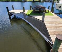 there is a boat docked at the end of a dock with grass on it and another boat in the background