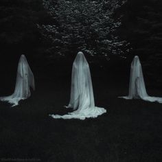 three ghostly people standing in the dark with long veils on their heads and body