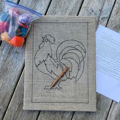 a small bag with a rooster drawn on it next to some crochet hooks