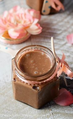 a glass jar filled with chocolate frosting sitting on top of a table next to flowers