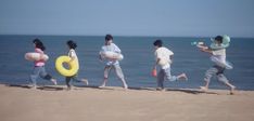 four people are running on the beach with inflatable toys around their ankles and one person is holding a water bottle