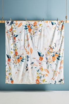 an orange and white flowered curtain hanging on a clothes line against a blue wall