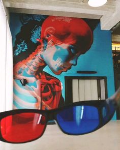 the reflection of a person wearing sunglasses in front of a wall with a painting on it