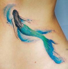 a woman's stomach with a blue and green mermaid tail tattoo on it,