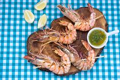 grilled shrimp on a wooden platter with dipping sauce and lemon wedges next to it