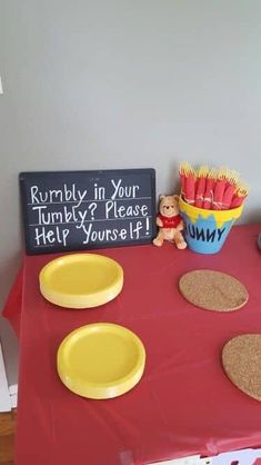 a red table topped with yellow plates and bowls filled with food next to a chalkboard sign