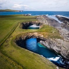 an aerial view of the ocean and cliffs with blue water in it, along with green grass