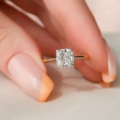 a woman's hand holding an engagement ring with a square diamond on the side