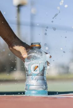 a person is touching a water bottle on a tennis court as it splashes around