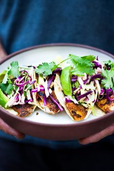 a person holding a plate with three tacos on it and garnished with cilantro