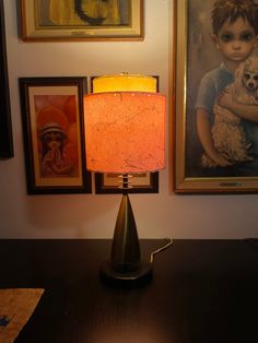 a lamp sitting on top of a wooden table next to pictures and paintings above it