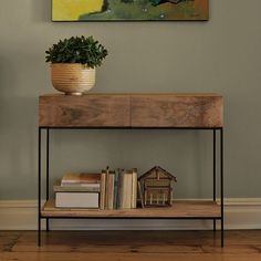 a painting on the wall above a table with books and a potted plant next to it