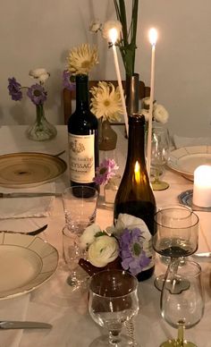 the table is set with wine bottles, candles and flowers in vases on it