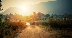 a jeep driving down a dirt road with the sun setting