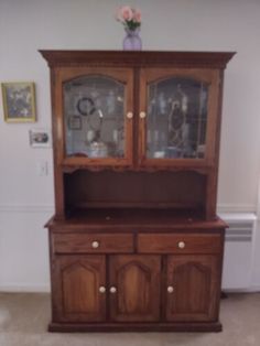 a wooden china cabinet with glass doors and drawers in the middle of a living room