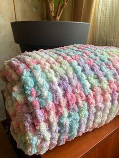 a crocheted blanket sitting on top of a wooden table next to a potted plant