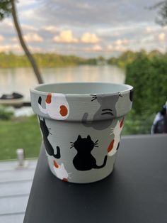 a cup with cats on it sitting on a table next to the water and trees