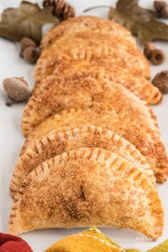 several pastries are lined up on a white surface next to some leaves and nuts