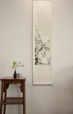 a painting hanging on the wall next to a stool and table with a plant in it