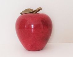 a red apple sitting on top of a white table next to a brown bird figurine