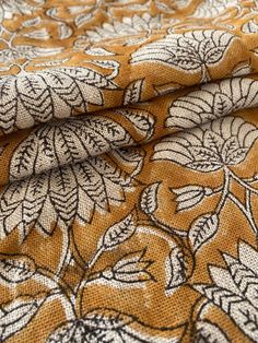 an orange and white flowered fabric with black leaves on it's side,