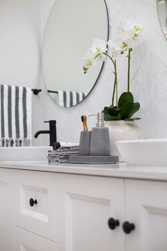 a white bathroom sink sitting next to a mirror with flowers in it and towels on the counter