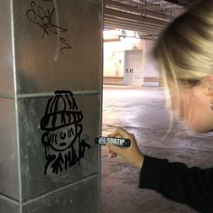 a woman writing graffiti on the side of a metal box in an empty parking garage