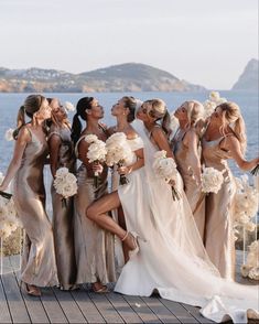 a group of women standing next to each other in front of the ocean holding bouquets