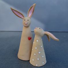 two ceramic rabbits are standing next to each other on a table, one is holding a heart