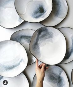 a person is holding some plates in front of the wall with black and white designs on them