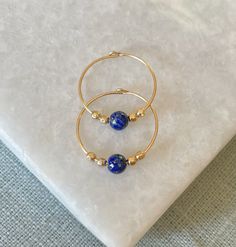 Vibrant blue lapis lazuli stones hung on delicate gold filled hoops. Lapis lazuli is known as the stone of friendship. They are super easy to put in and comfortable to wear all day. Each hoop measures 15mm in diameter and they are available in gold filled or sterling silver. Each pair comes beautifully gift wrapped. Lapis Lazuli is one of the most sought after stones in use since man's history began. Its deep, celestial blue remains the symbol of royalty and honour, gods and power, spirit and vision. It is a universal symbol of wisdom and truth. Gold filled is made by heat and pressure bonding a layer of karat gold to a metal core. Unlike gold plated, gold filled has an actual layer of karat gold, not just a microscopic film and with the proper care will last a lifetime. I am committed to Handmade Lapis Lazuli Jewelry For Everyday, Blue Hoop Brass Jewelry, Blue Hoop Jewelry With Natural Stones, Blue Brass Hoop Jewelry, Blue Natural Stone Hoop Jewelry, Dainty Blue Hypoallergenic Hoop Earrings, Blue Dainty Hypoallergenic Hoop Earrings, Blue Brass Hoop Earrings As Gift, Blue Tarnish Resistant Hoop Earrings