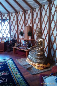 there is a gold buddha statue in the middle of a room with white walls and wood flooring