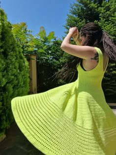 a woman in a bright yellow dress is standing near some bushes and looking off into the distance