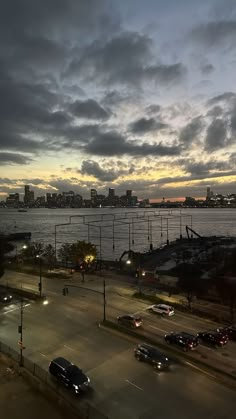 cars are driving on the road near an ocean and cityscape at night time