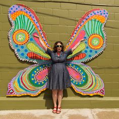 a woman standing in front of a green wall with a colorful butterfly wings on it