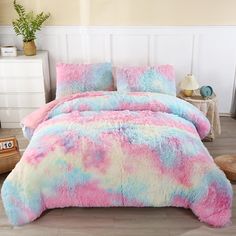 a bed covered in pink, blue and white fluffy comforter next to a night stand