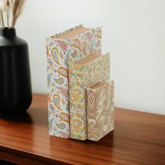 two books sitting on top of a wooden table next to a vase with feathers in it