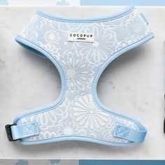 The Luxe Adjustable Neck Harness in Baby Blue Flower by Cocopup London showcases an elegant white ornate floral pattern on a baby blue background. A small white tag at the center displays the brand name, adding a touch of sophistication. This adjustable neck harness is situated on a light marble surface, making it a refined addition to your dog's accessories collection. Cute Leashes For Dogs, Cocopup London, Doggie Clothes, Puppy Things, Cute Dog Harness, Luxe Baby, Room Things, Dogs Stuff, Small Dog Harness