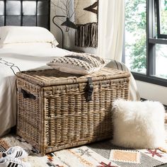 a wicker trunk on the floor in front of a bed with pillows and blankets