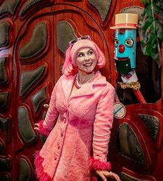 a woman dressed in pink standing next to a wooden door with a face painted on it