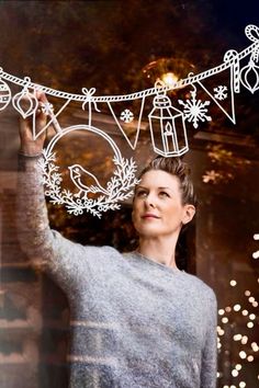 a woman standing in front of a window with christmas decorations hanging from it's sides