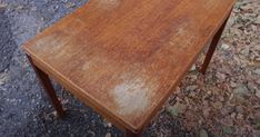 an old wooden table sitting in the middle of some leaves on the ground and dirt