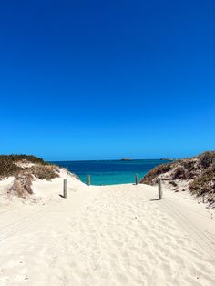 a sandy path leading to the ocean on a sunny day with clear blue skies in the background