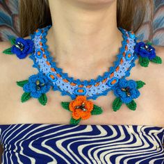 a woman wearing a blue and orange crochet necklace with flowers on the front