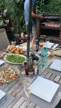 an outdoor table with food and drinks on it, including salads and wine glasses